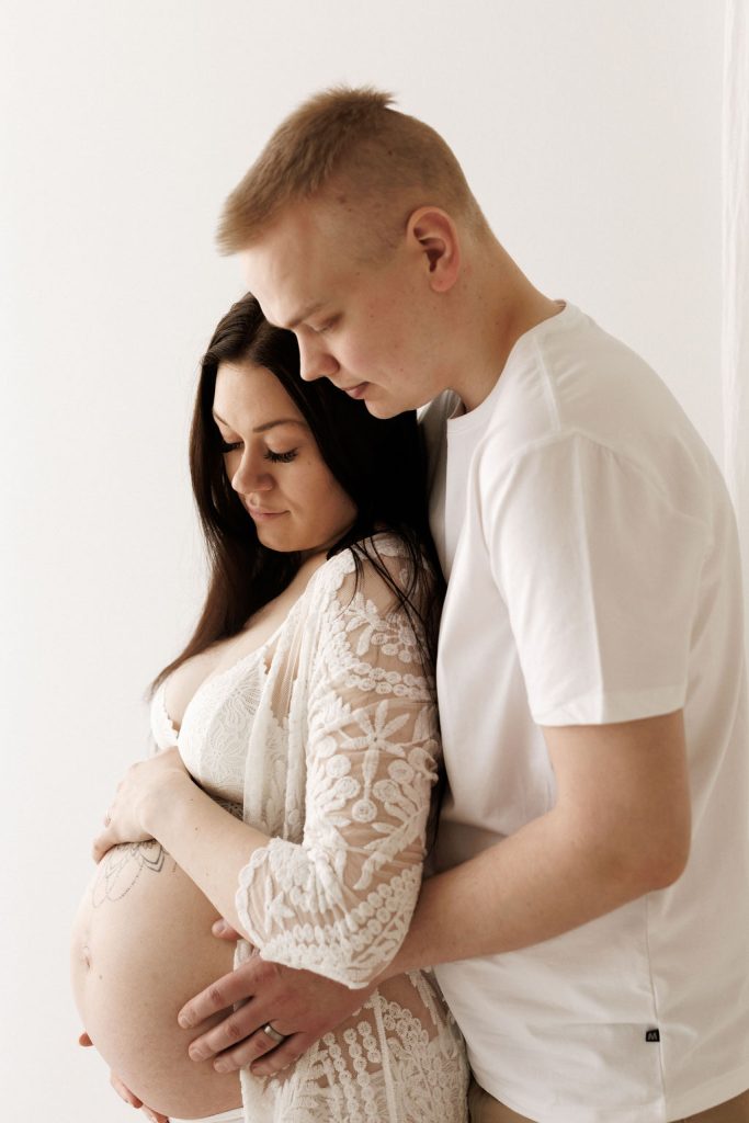 Raskaana olevan naisen ja puolison odotuskuvaus Jyväskylässä – pariskunta halailee vatsaa.